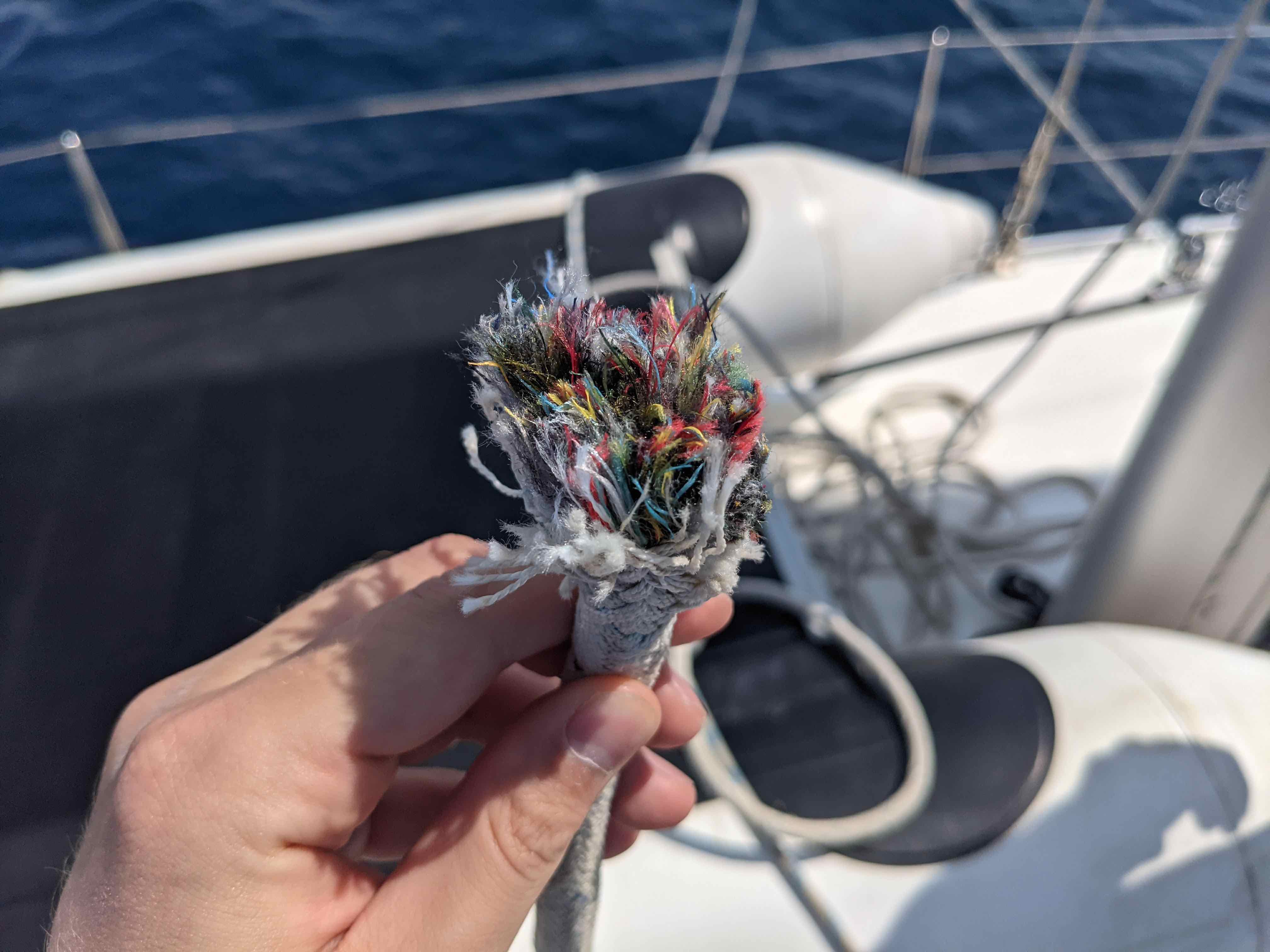 Hand holding the end of a torn halyard that is significantly chafed